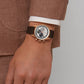 Brown leather strap watch on a wrist, featuring a white dial with black subdials and red accents.
